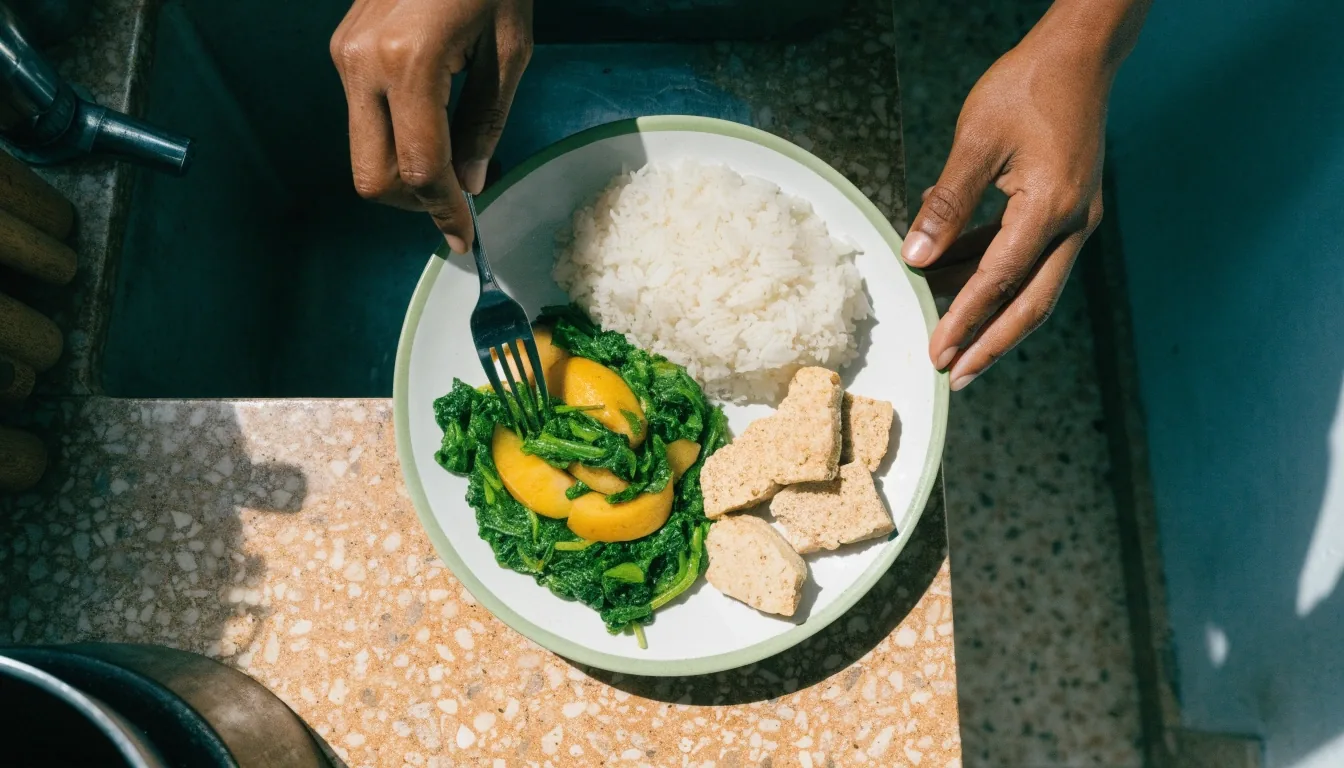 A home-cooked plate being assembled with rice, tempeh, greens and fish on a terrazzo countertop